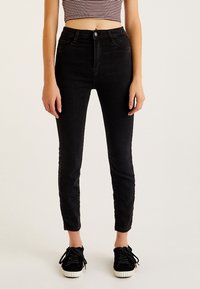 Jeans ajustados de tiro alto en color negro, hechos de denim, con cierre de botón en la parte delantera, bolsillos laterales y traseros, y un corte slim.