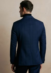 Granatowa marynarka garniturowa o dopasowanym kroju z delikatnym wzorem w kratę, gładką teksturą i kontrastowym czarnym kołnierzykiem, widoczna z tyłu.