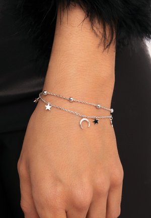 Silberne Kettenarmband mit Stern- und Halbmondanhängern, das runde Perlen und ein filigranes Design aufweist, getragen an einer Hand.
