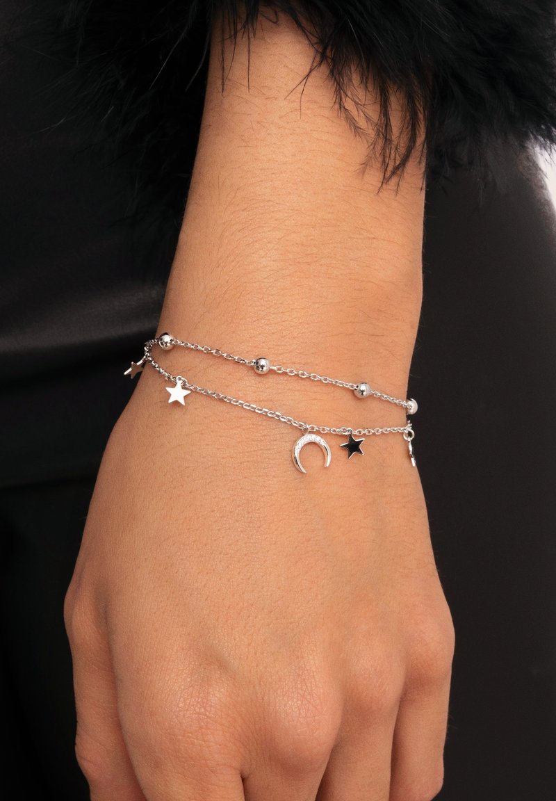 Pulsera de cadena de plata con charms de estrella y luna creciente, que presenta cuentas redondas y un diseño delicado, llevada en una mano.