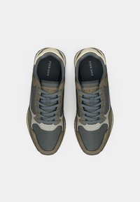 Gray and olive green sneakers with textured material, padded collar, and lace-up design. Features cream accents and a sleek shape.