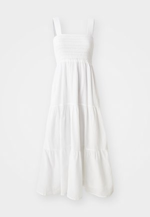 Hvit midi-kjole med smock-bodice, brede skulderstropper og lagdelt design med flytende hemline. Laget av lett materiale.
