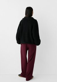 Sweater noir en tricot surdimensionné avec un large col, associé à un pantalon large bordeaux. Texture lisse et silhouette décontractée.