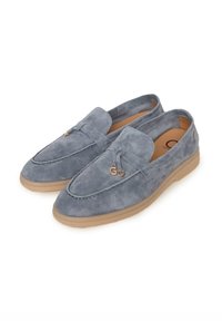 Paire de mocassins en daim gris avec semelles en caoutchouc beige, ornés de pampilles décoratives et de breloques dorées sur fond blanc.