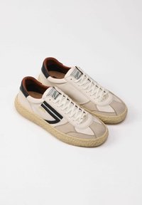 Sneaker in pelle beige con una finitura testurizzata, dettagli neri, lacci bianchi e una suola spessa in corda naturale. Presenta un'etichetta del marchio retrò.