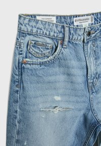 Vaqueros de denim desgastado en azul claro con bolsillo frontal, bolsillo para monedas, remaches de metal y etiqueta de marca Stradivarius en la cintura.