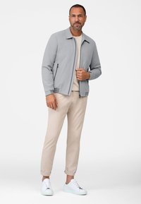 Lys grå bomberjakke med lynlås foran, ribbede manchetter og krave, parret med beige chinos og hvide sneakers.