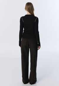 Femme de dos portant un top noir à manches longues côtelé avec des bandes blanches aux épaules et un pantalon large noir avec un subtil imprimé léopard.