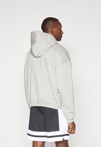 Hætte sweatshirt i lys grå, lavet af bl�ødt stof. Har en afslappet pasform med faldne skuldre og ribbede manchetter. I kombination med sorte shorts.