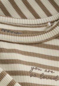 Beige en bruine ribgebreide stof met horizontale strepen en gedeeltelijke tekst "je bent" geborduurd in donkere draad.