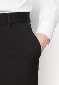 Pantalones negros de tejido de mezcla de algodón, con una textura suave, bolsillo lateral y una cintura limpia con un discreto detalle de costura.