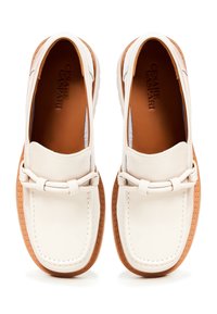 Mocassins en cuir blanc avec une semelle en caoutchouc marron. Comprend une sangle décorative à l'avant avec un détail en nœud. Texture lisse et forme arrondie.