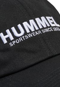Schwarze Kappe mit gebogenem Schirm, vorne mit weißem gestickten Text "HUMMEL SPORTSWEAR SINCE 1923". Strapazierfähiges Material aus Baumwolle, einfaches Design.