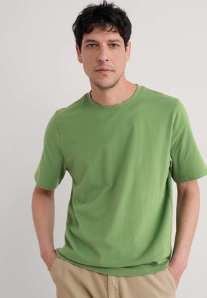 Grünes Baumwoll-T-Shirt mit kurzen Ärmeln, Rundhalsausschnitt und lockerer Passform. Glatte Textur ohne sichtbare Muster oder Akzente.