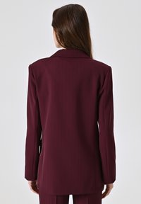 Bordeaux gestreepte blazer met een enkele split, notch lapel en lange mouwen, gemaakt van een gladde stof. Achteraanzicht met lichte schoudervulling.