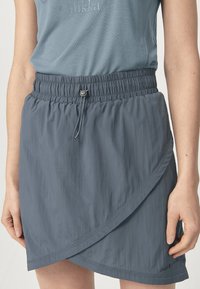 Grijze, lichte wikkelrok met een elastische tailleband, verstelbaar trekkoord en een gladde textuur. Heeft een diagonale zoom en subtiele branding.