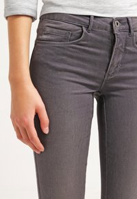 Pantalones vaqueros grises de denim con un ajuste slim, diseño de cinco bolsillos y un ligero estiramiento. Presentan un cierre de botón y detalles sutiles de costura.