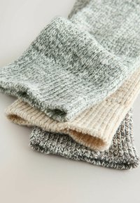 Tre strikede stykker stof i grå, beige og off-white, hver med ribbet tekstur og rullede kanter, stablet på en flad overflade.