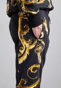 Melni sporta bikses ar zelta viļņveida rakstiem, ar sānu kabatu. Audums izskatās mīksts, ar brīvu piegriezumu un elastīgu jostasvietu.