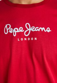 Piros póló, amelyen fehér "Pepe Jeans London" logó látható a mellkasi részen.