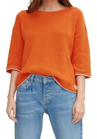 Suéter naranja de punto con mangas hasta el codo, con un tejido acanalado texturizado y dobladillo en contraste. Combinado con jeans de mezclilla azul claro.