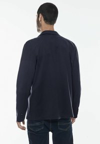 Marinblå kavaj med skräddarsydd passform, enfacksdesign, insvängda slag och knappar vid ärmarna. Slät tyg med en subtil textur.