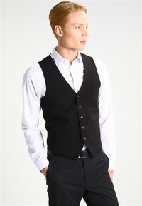 Schwarze Weste mit sechs Knöpfen, getragen über einem weißen Hemd mit blauen Punkten, kombiniert mit dunklen Hosen und einem schwarzen Gürtel.