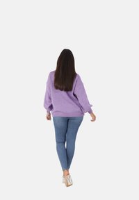 Maglione viola lavorato a maglia con maniche oversize, abbinato a jeans blu aderenti e sandali con tacco argento, visto da dietro.