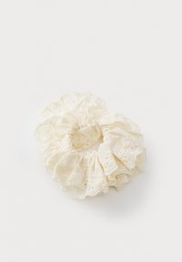 Kreemikas värvitooni kangast scrunchie, millel on rippuv disain, millel on lilleline tikand ja lõigatud detailid äärtes.