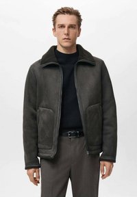 Giacca in suede grigio scuro con zip frontale, colletto morbido e due grandi tasche anteriori. Texture morbida e vestibilità rilassata.