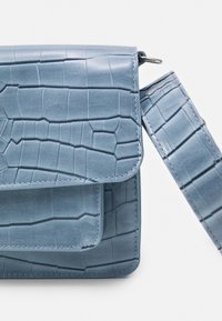 Blå faux läder axelväska med krokodilstruktur, vikbar lockflap och en justerbar rem. Har ton-i-ton sömnad och stilren hårdvara.