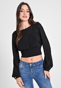 Schwarze, kurze Bluse mit langen, puffigen Ärmeln, aus leichtem Stoff gefertigt. Sie hat eine taillierte Taille und Knopfakzente an den Ärmelabschlüssen.