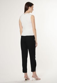 Top blanco sin mangas con un diseño ajustado, combinado con pantalones negros ajustados que presentan detalles de botones en los puños y sandalias de tacón blanco abiertas por delante.