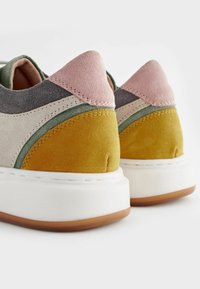 Mehrfarbige Sneaker mit einer Kombination aus Wildleder-Patches: Gelb, Grün, Rosa und Grau. Ausgestattet mit einer weißen Sohle und kontrastierenden strukturierten Akzenten.