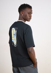 Black cotton t-shirt featuring a multi-colored graphic print on the back, with a round neckline and short sleeves.