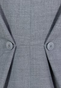 Grijs stof met een fijne textuur heeft twee grijze knopen op een patte, die een hoekig ontwerp en op maat gemaakte plooi-details benadrukken.