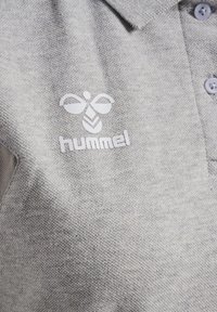 Ljusgrå pikétröja i texturerat tyg med en liten vit logotyp och tre knappar vid kragen, med en klassisk passform.