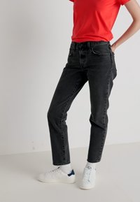 Jeans in denim nero con taglio dritto, vita alta, cinque tasche e leggera sbiaditura, abbinati a una maglietta rossa a maniche corte e scarpe da ginnastica bianche.