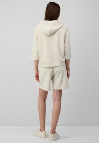 Hellbeige Hoodie mit kurzen Ärmeln und Kapuze, kombiniert mit passenden Shorts. Beide Kleidungsstücke besitzen eine glatte, weiche Textur und ein minimalistisches Design.