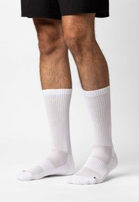 Calze sportive bianche con texture a coste, lunghezza a crew, punta e tallone rinforzati, e pannelli in rete per traspirabilità.