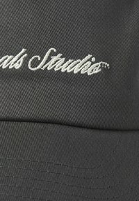 Black cap made of textured fabric featuring embroidered "Studio" logo in white; curved visor and visible stitching detail.