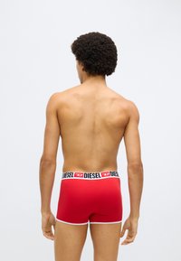 Sarkani bokseršorti ar elastīgu melnu jostas daļu, uz kuras baltā krāsā ir uzraksts "DIESEL". Gluda tekstūra, pieguļošs dizains ar baltu apdari gar kāju malām.