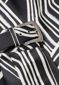 Black and white striped fabric featuring a silver metal buckle on a belt, with visible stitching and a soft, smooth texture.