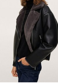 Veste en cuir noir avec col en fausse fourrure grise, fermeture éclair à l'avant et coupe décontractée. Caractéristiques : manches larges et contraste textural subtil.