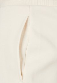 Tejido de color beige claro con una textura suave que presenta un detalle de bolsillo lateral. La cinturilla es acanalada para mayor comodidad.