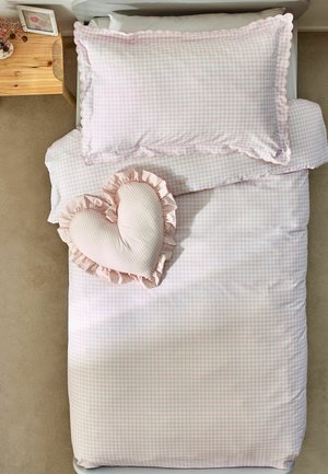 Einzelbett mit rosa-weiß kariertem Bettzeug und einem gerafften herzförmigen Kissen auf beigem Teppich neben einem hölzernen Nachttisch.
