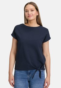 Marineblå kortærmet top med rund halsudskæring, tekstureret stof og en knyttet detalje i taljen, parret med lyseblå denim.
