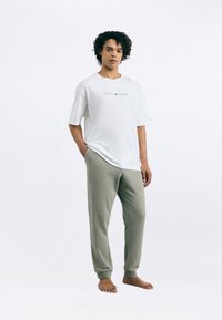 Hvid t-shirt med "TOMMY HILFIGER" logo, parret med grågrønne sweatpants. T-shirten har en afslappet pasform; sweatpantsene har ribbede manchetter.