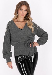 Pulover gri cu mâneci lungi, având accente perlate pe umeri și o panglică la talie. Asortat cu pantaloni negri lucioși.