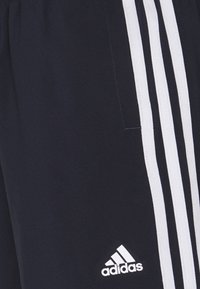 Pantalones cortos azul marino con tres rayas verticales blancas en los lados, hechos de tela suave con un logotipo de Adidas en la esquina inferior.